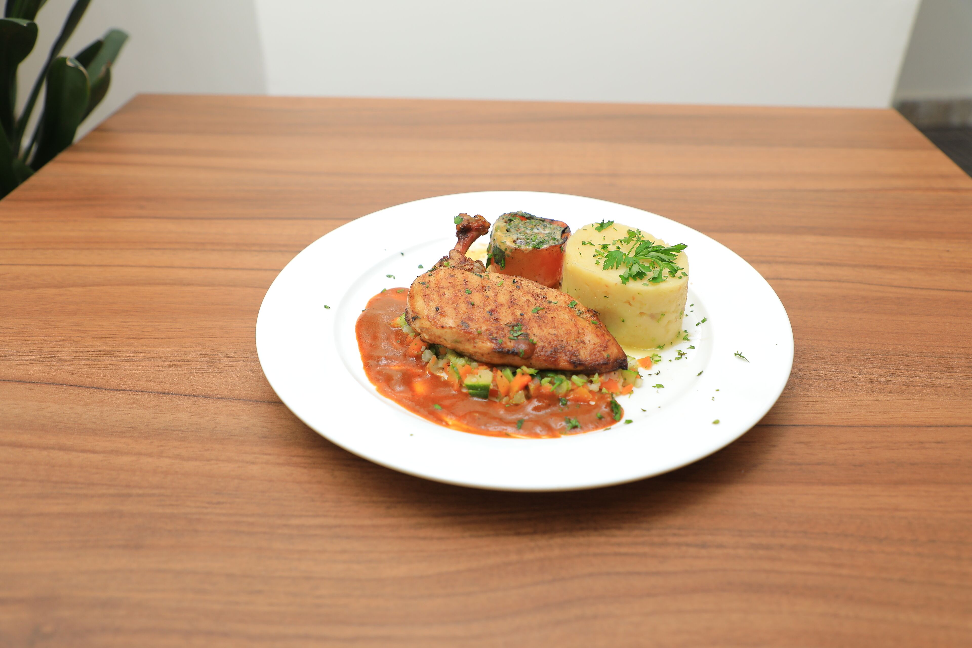 A plate with a piece of meat, a vegetable, and a mashed potato on a wooden table.