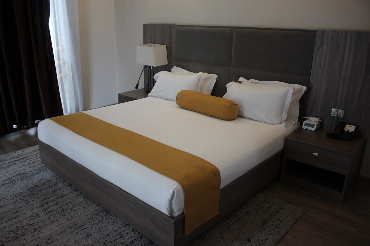 A hotel room with a large bed, a nightstand with a lamp, and a bedside table with a phone and a power outlet.