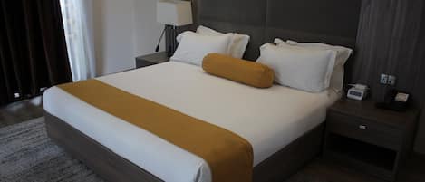 A hotel room with a large bed, a nightstand with a lamp, and a bedside table with a phone and a power outlet.