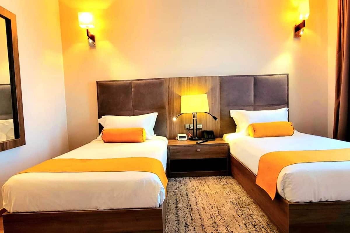 A hotel room with two beds, a large mirror, bedside lamps, and a nightstand.