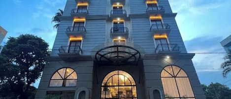 Et hotel med flere etager, symmetrisk facade, stor buet indgang og ensartede altaner.