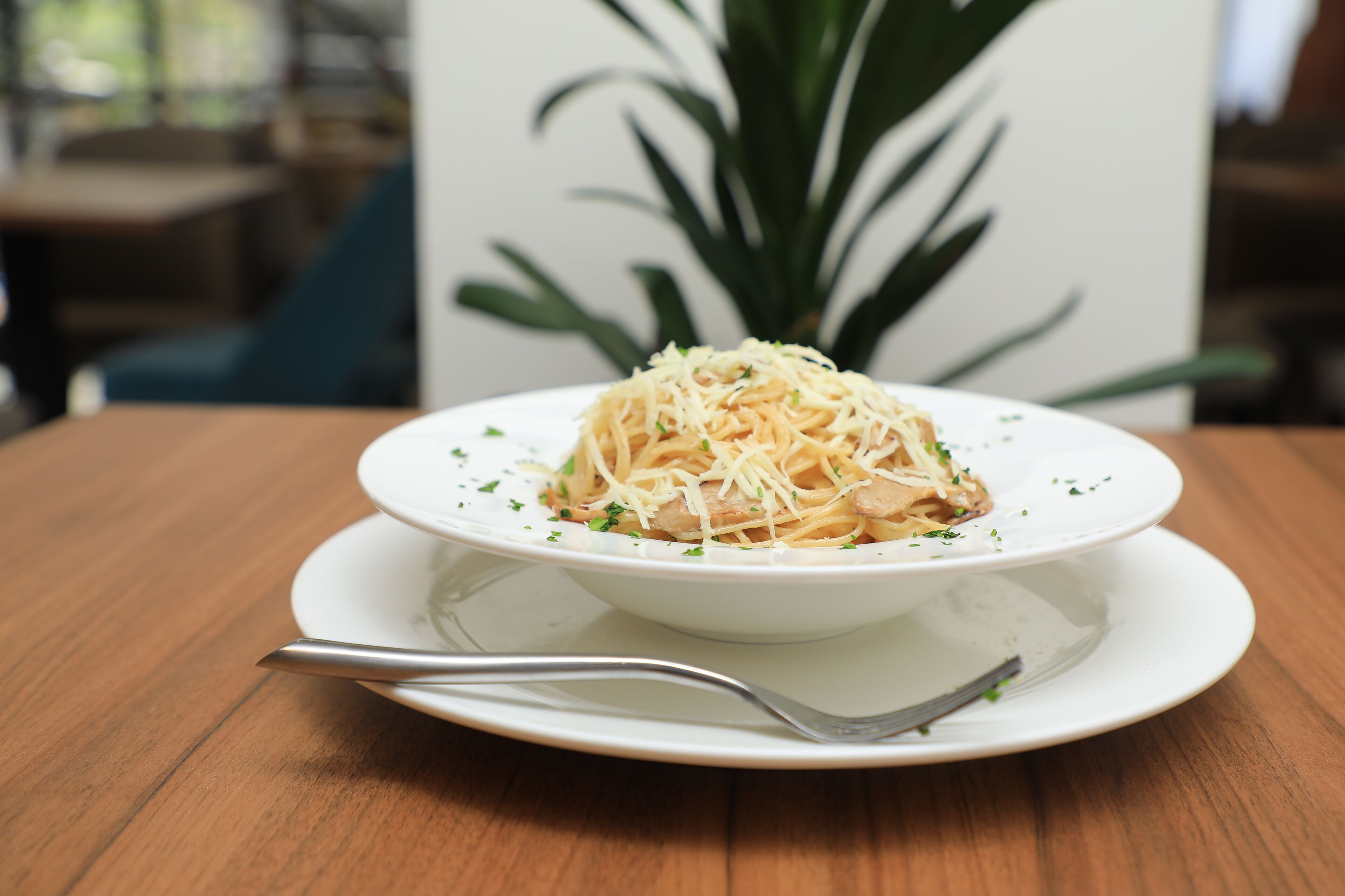 A plate of spaghetti with cheese on a white plate on a wooden table.