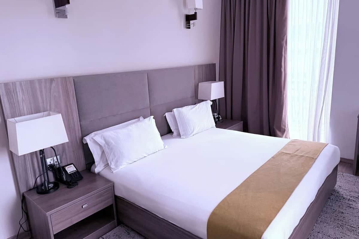 A hotel room with a large bed, two bedside tables, a nightstand, and a window with curtains.