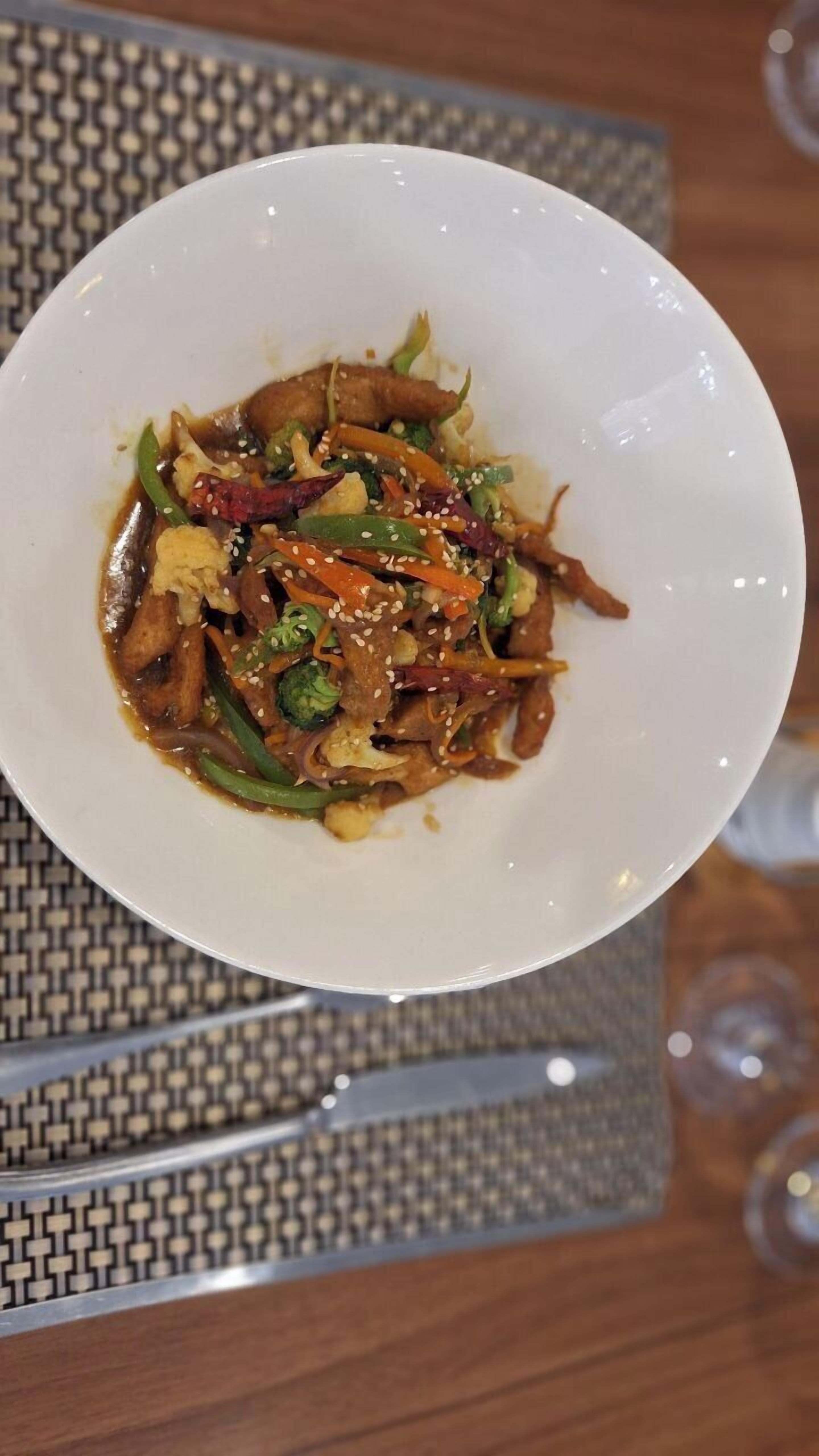 A bowl of stir-fried vegetables and meat on a white plate.