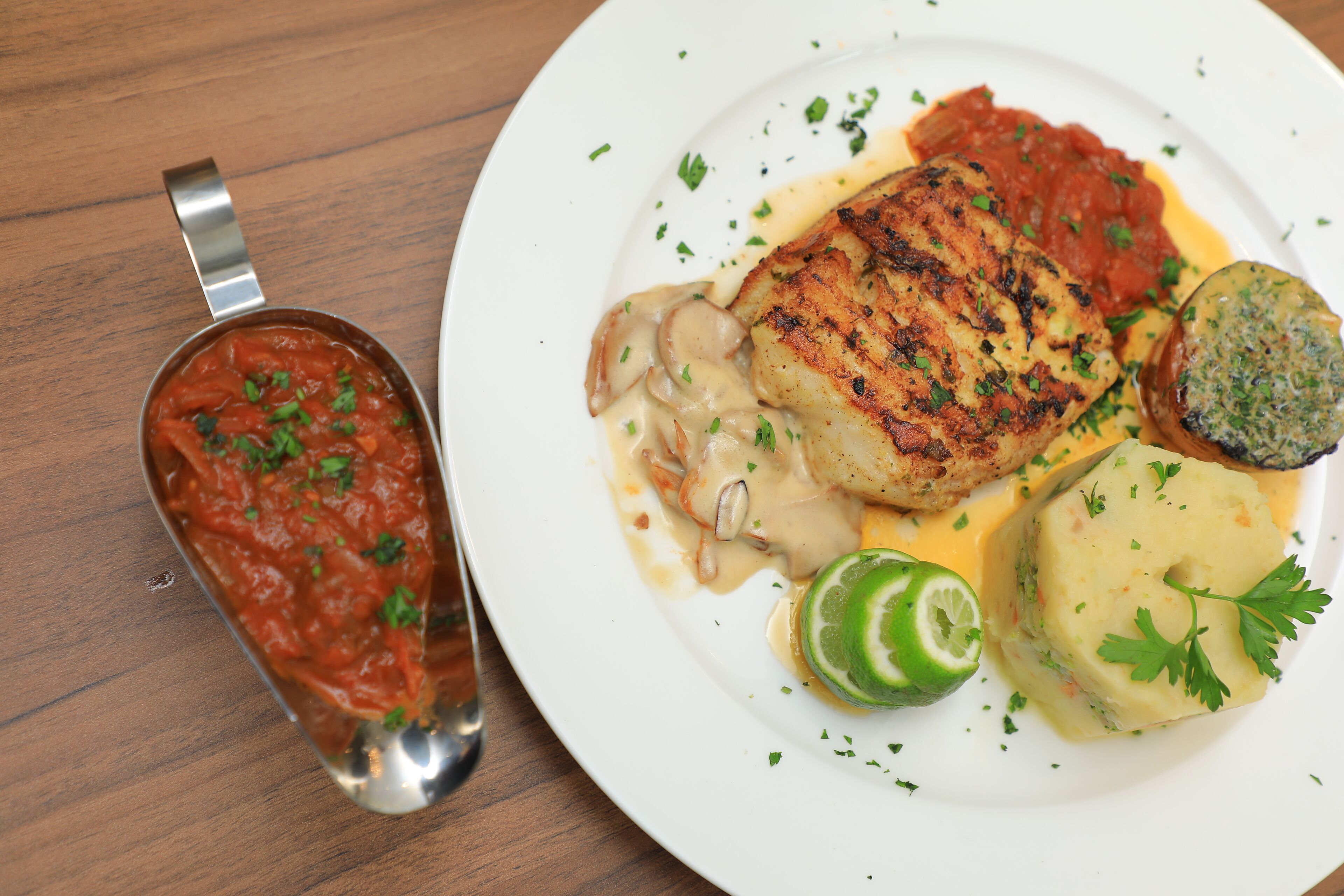 Un plato con pescado a la parrilla, puré de papas y salsa de tomate.