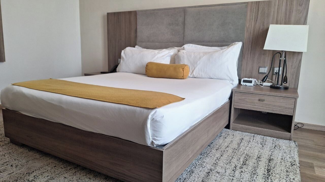 Ein Hotelzimmer mit einem großen Bett, einem Nachttisch mit Lampe und einer Steckdose.