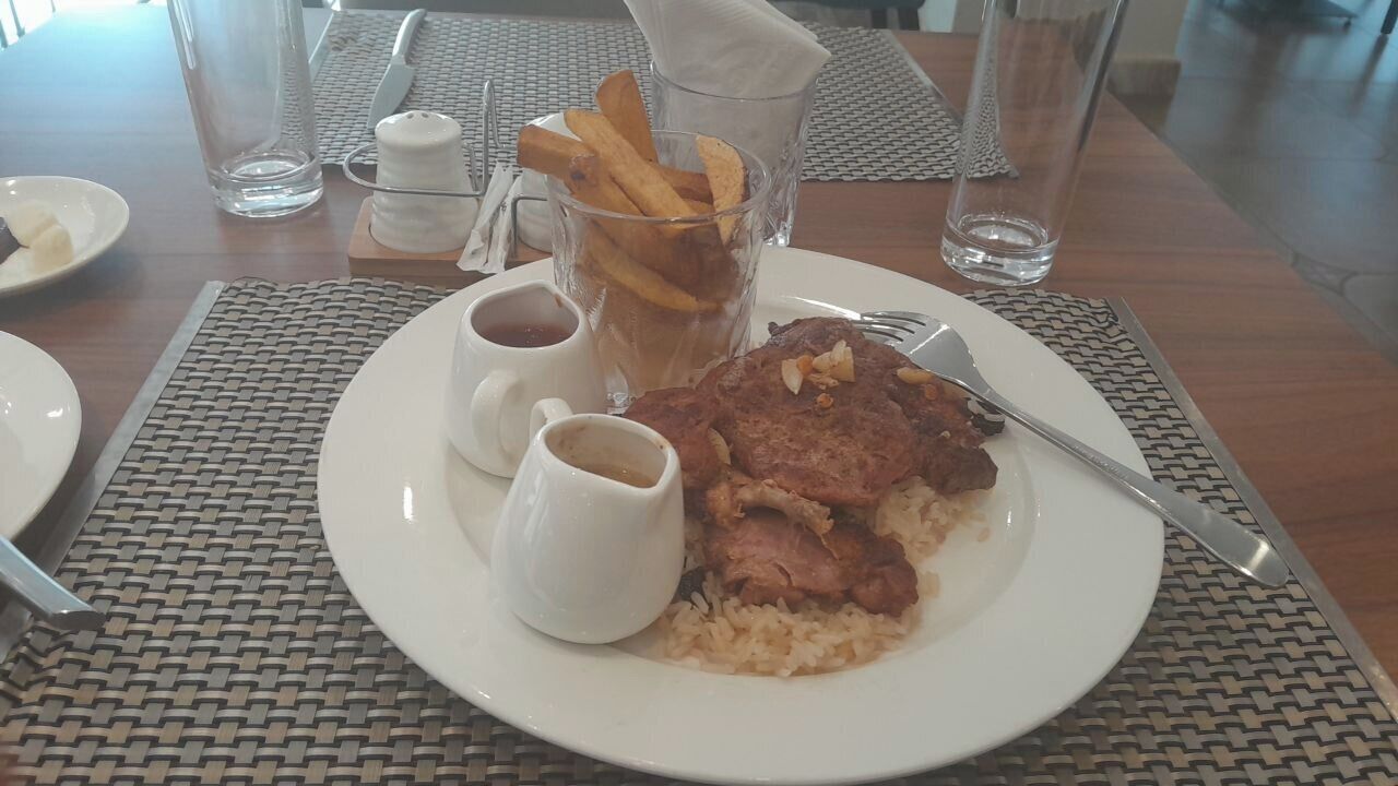 A dining table with a plate of food, including steak, rice, and fries, accompanied by two small cups of sauce.