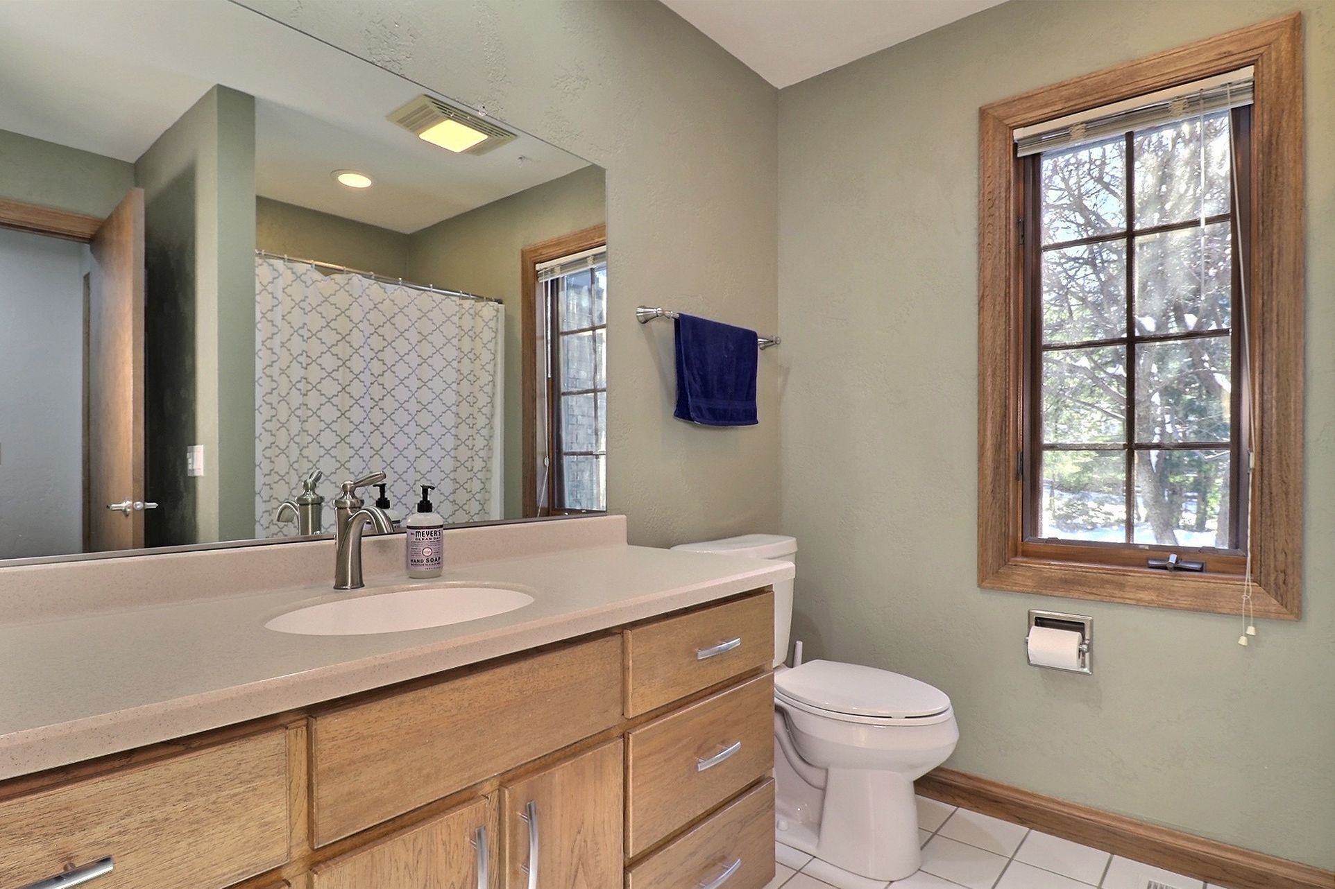 Une salle de bain avec un meuble-lavabo en bois, un évier, des toilettes et une fenêtre donnant sur les arbres.