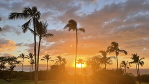 Un coucher de soleil sur un terrain de golf, avec des palmiers et un ciel dégagé.