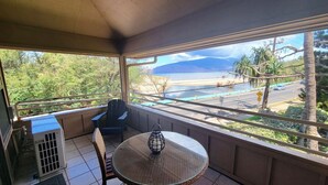 Een balkon met een tafel en stoelen, met uitzicht op een strand en een weg met een snelheidsbeperkingsbord.