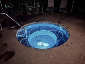 A circular hot tub with a mosaic design, surrounded by a concrete deck.