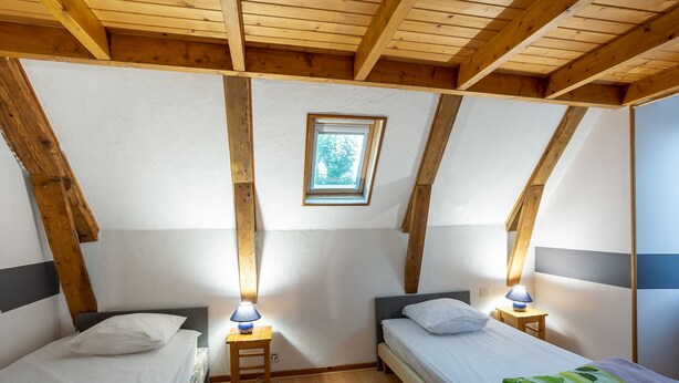 A bedroom with two single beds, wooden beams, a skylight, and a small table with a lamp. - Gite Les Marmottes - Two Bedroom House, Sleeps 5 (Trémouille)