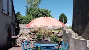 A patio with a table and chairs, a stone wall, and a tree in the background. - Gite Les Marmottes - Two Bedroom House, Sleeps 5 (Trémouille)