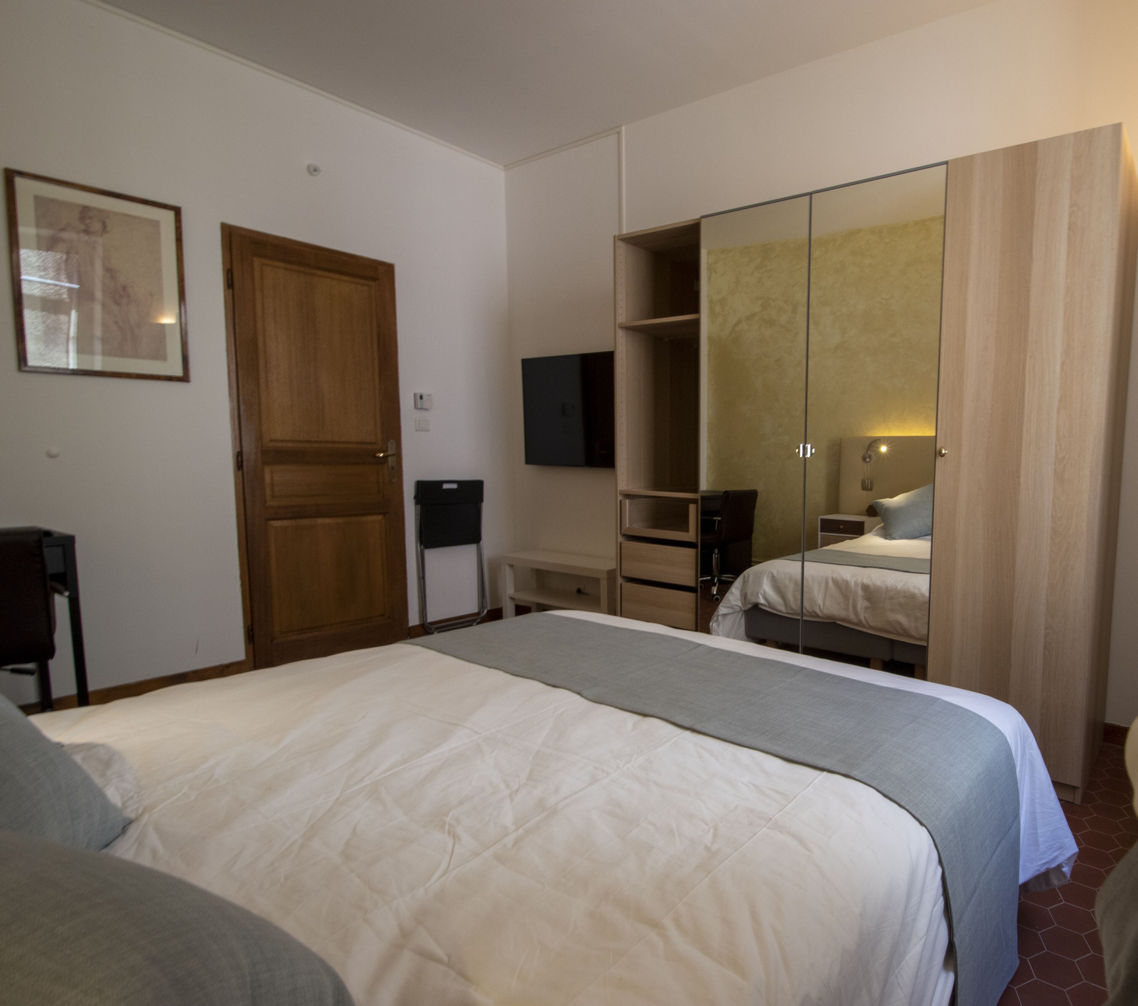 Una habitación de hotel con una cama grande, un armario, un televisor y un espejo.