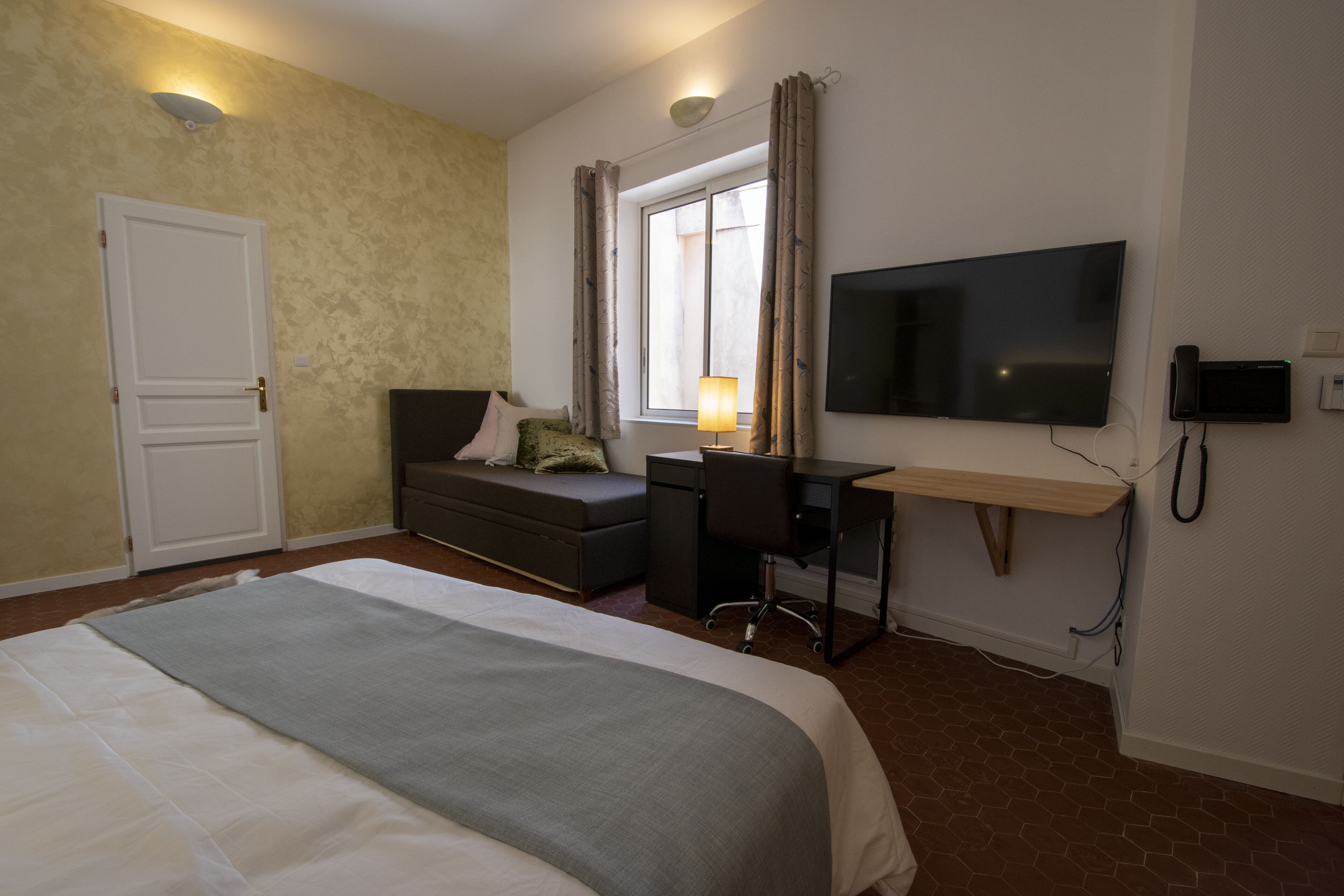 Une chambre d’hôtel équipée d’un lit, d’un bureau, d’une chaise, d’une télévision et d’une fenêtre avec des rideaux.