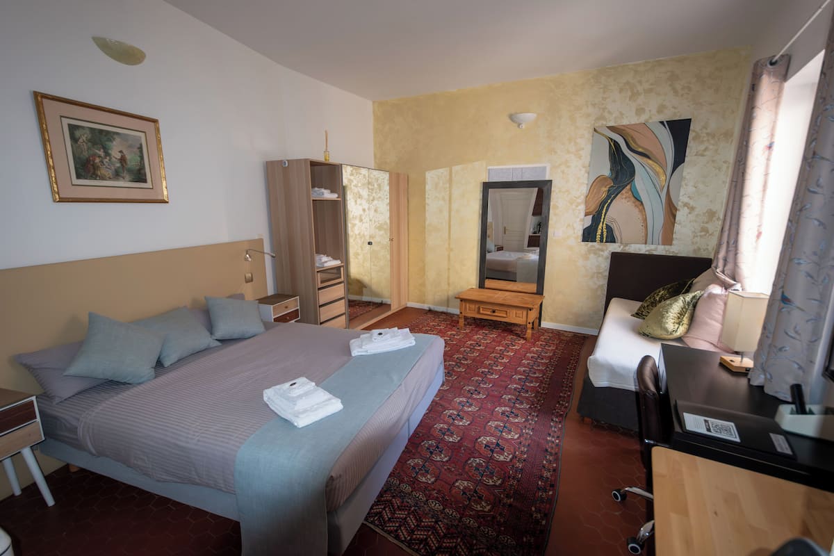 A hotel room with a bed, a desk, a wardrobe, a mirror, and a painting on the wall.