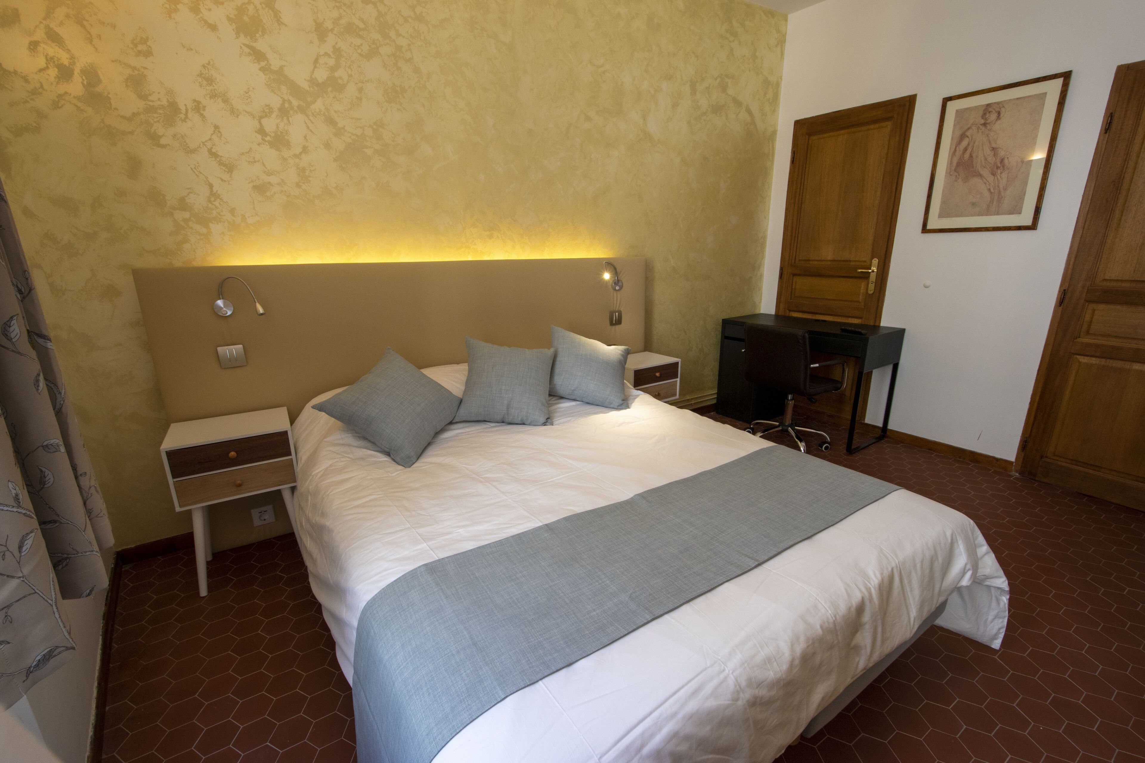 A hotel room with a large bed, a bedside table, a desk, and a chair.