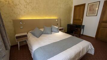 A hotel room with a large bed, a bedside table, a desk, and a chair.