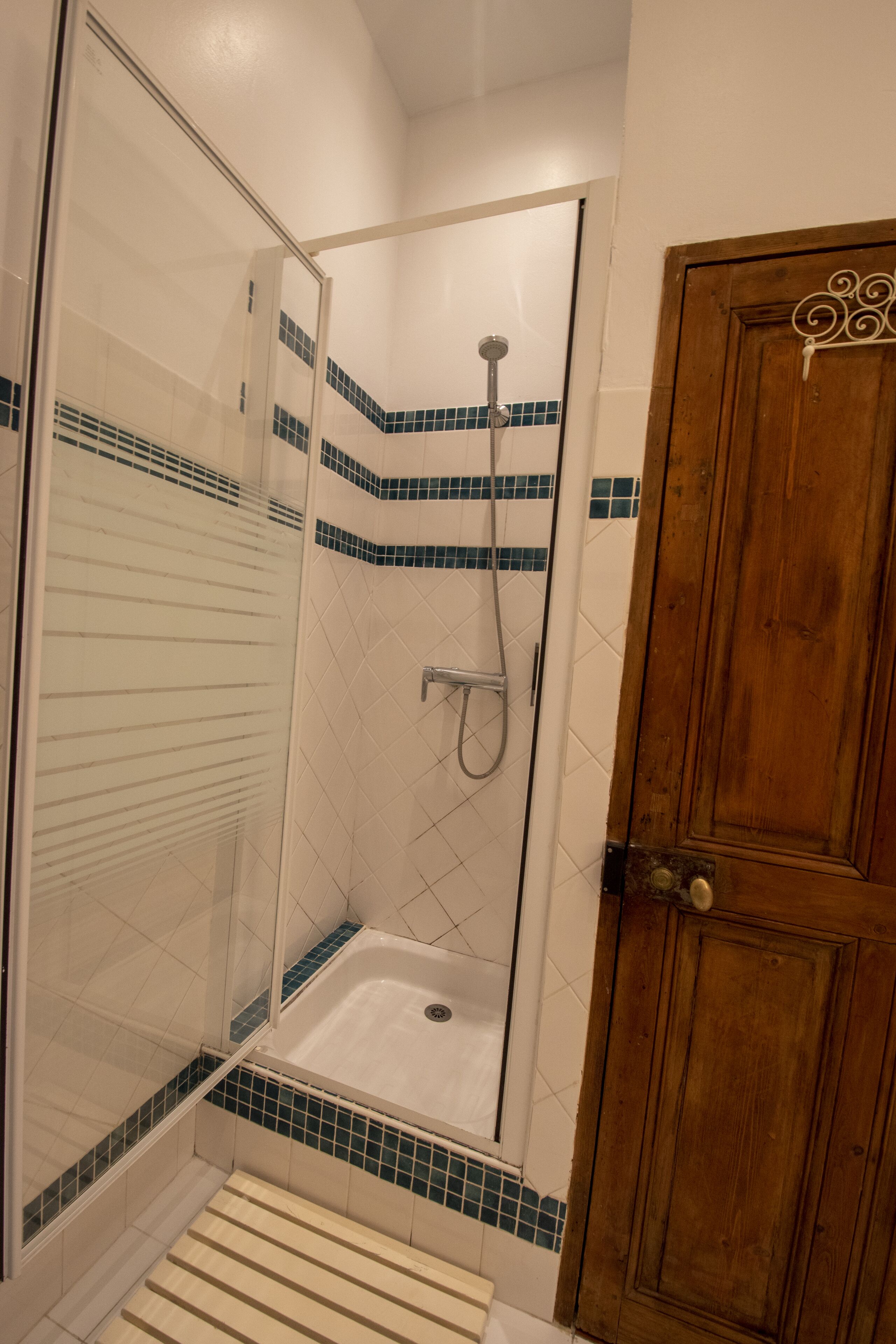 A shower with a glass door, a wooden door, and a tiled floor.