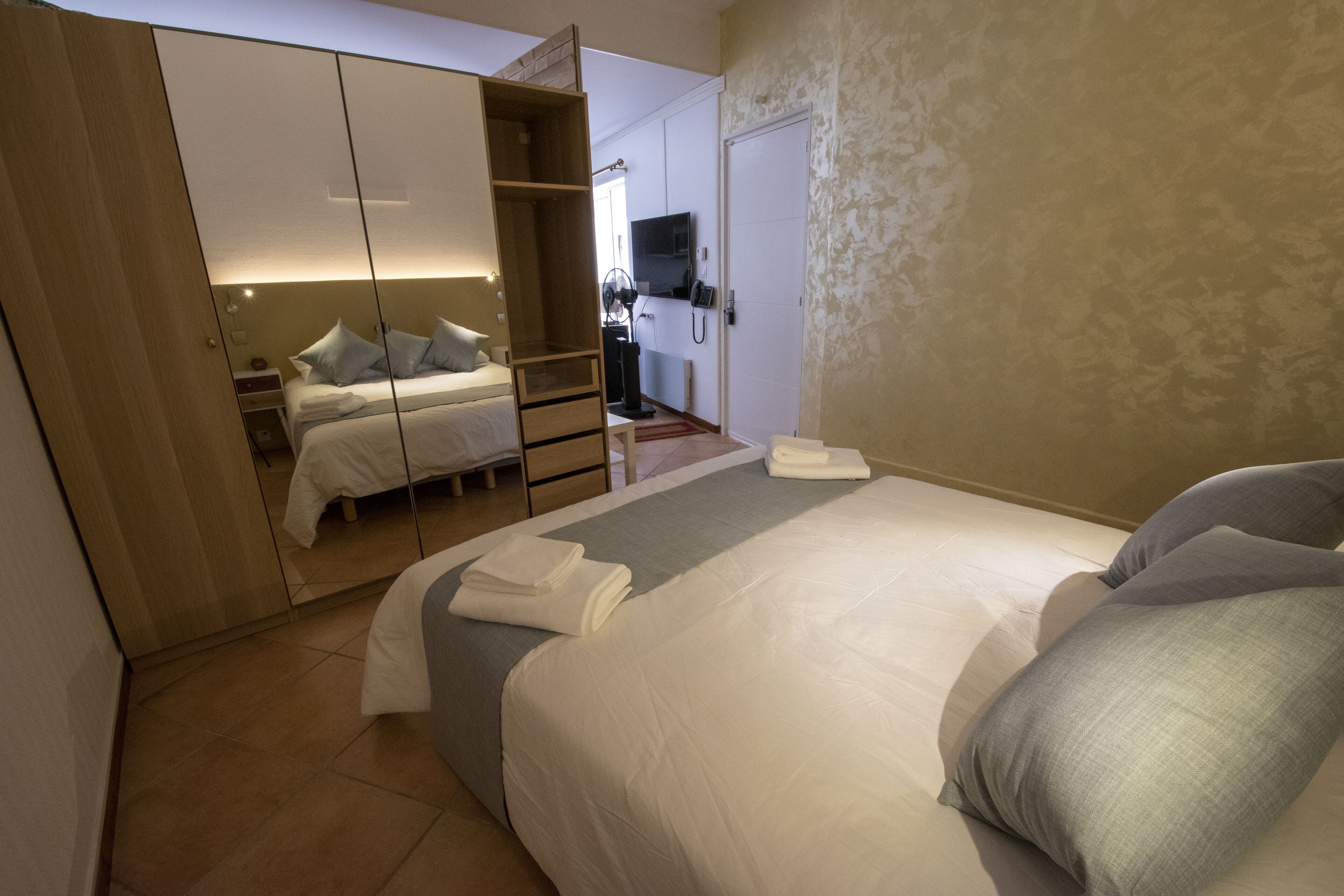 A bedroom with a bed, a wardrobe, a television, and a desk.