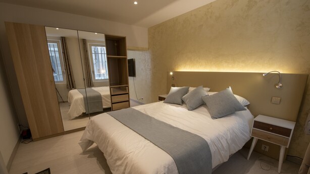 A bedroom with a large bed, bedside tables, a mirror, and a wardrobe. - A L'OMBRE DU PALAIS (Avignon)