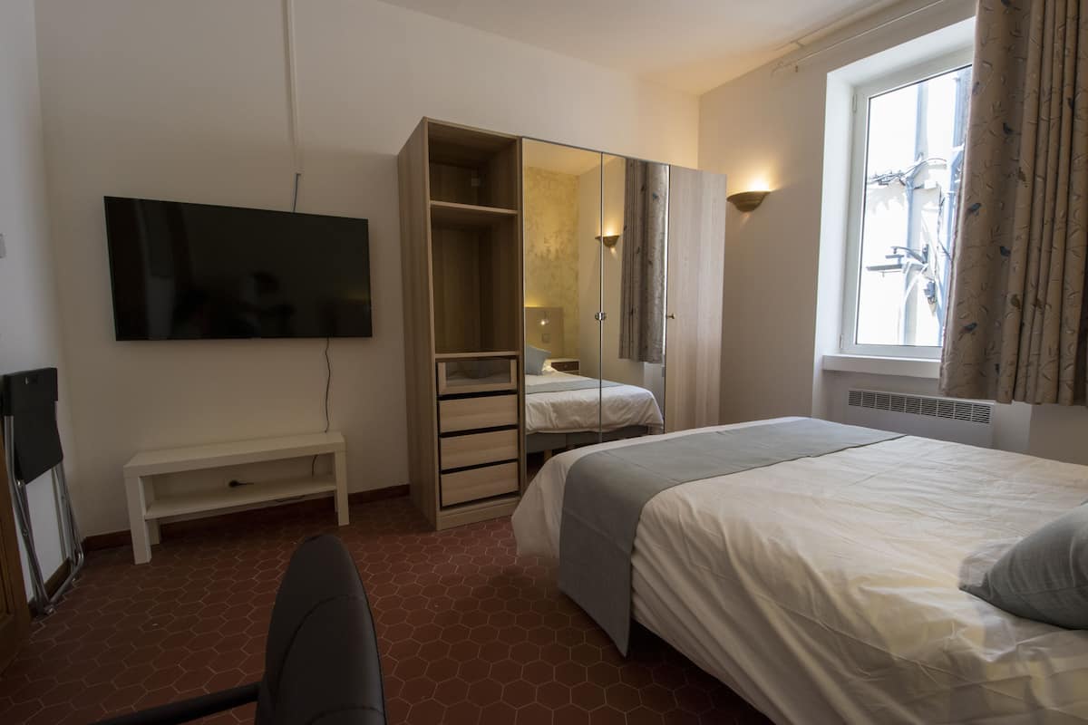A hotel room with a bed, a TV mounted on the wall, a wardrobe, and a window with curtains.