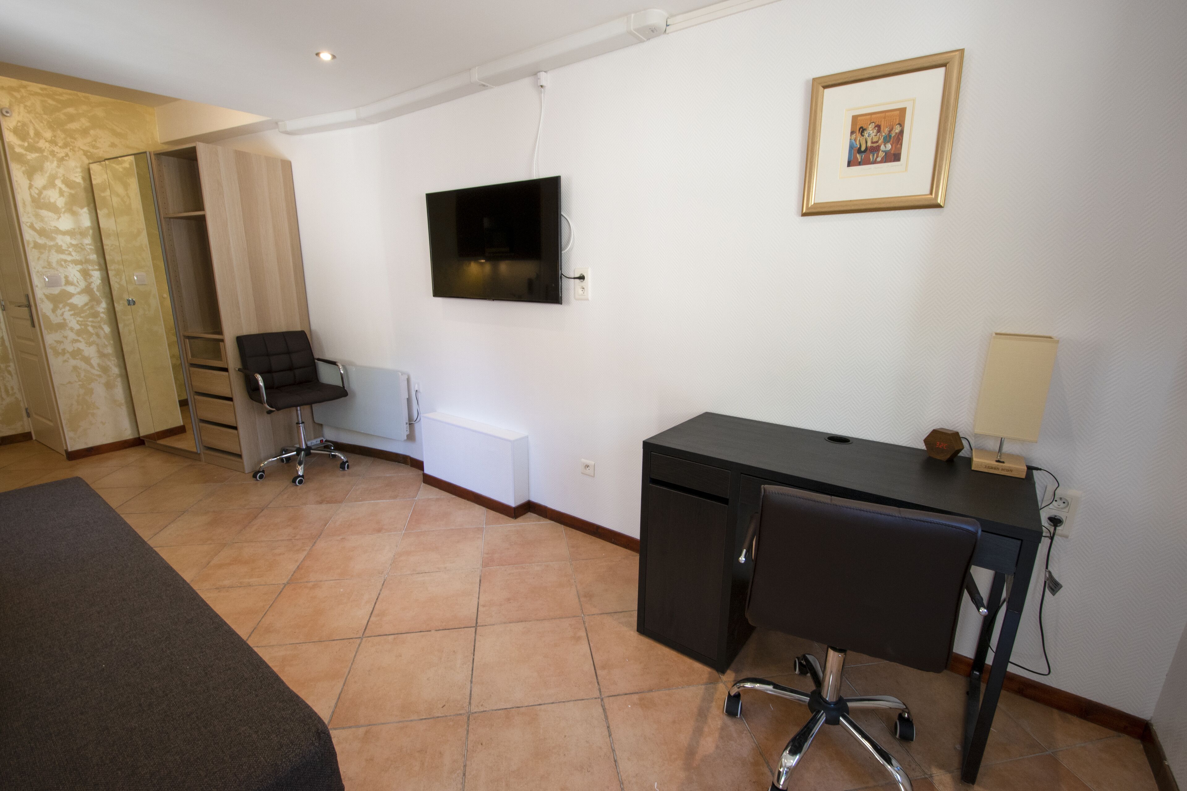 A room with a bed, a desk, a chair, a TV, and a wardrobe.