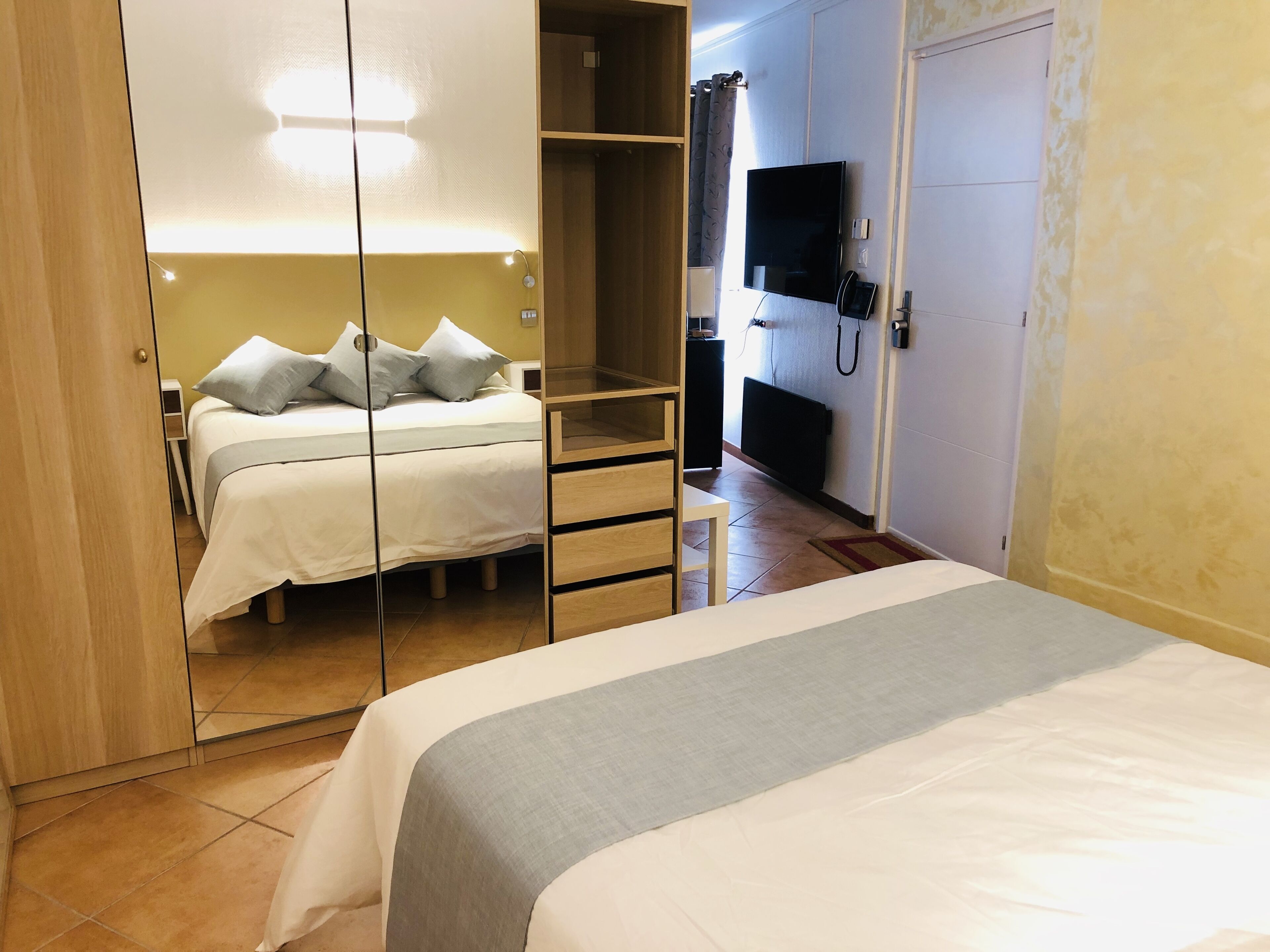 Une chambre d’hôtel avec un lit, une télévision, une armoire et un miroir.