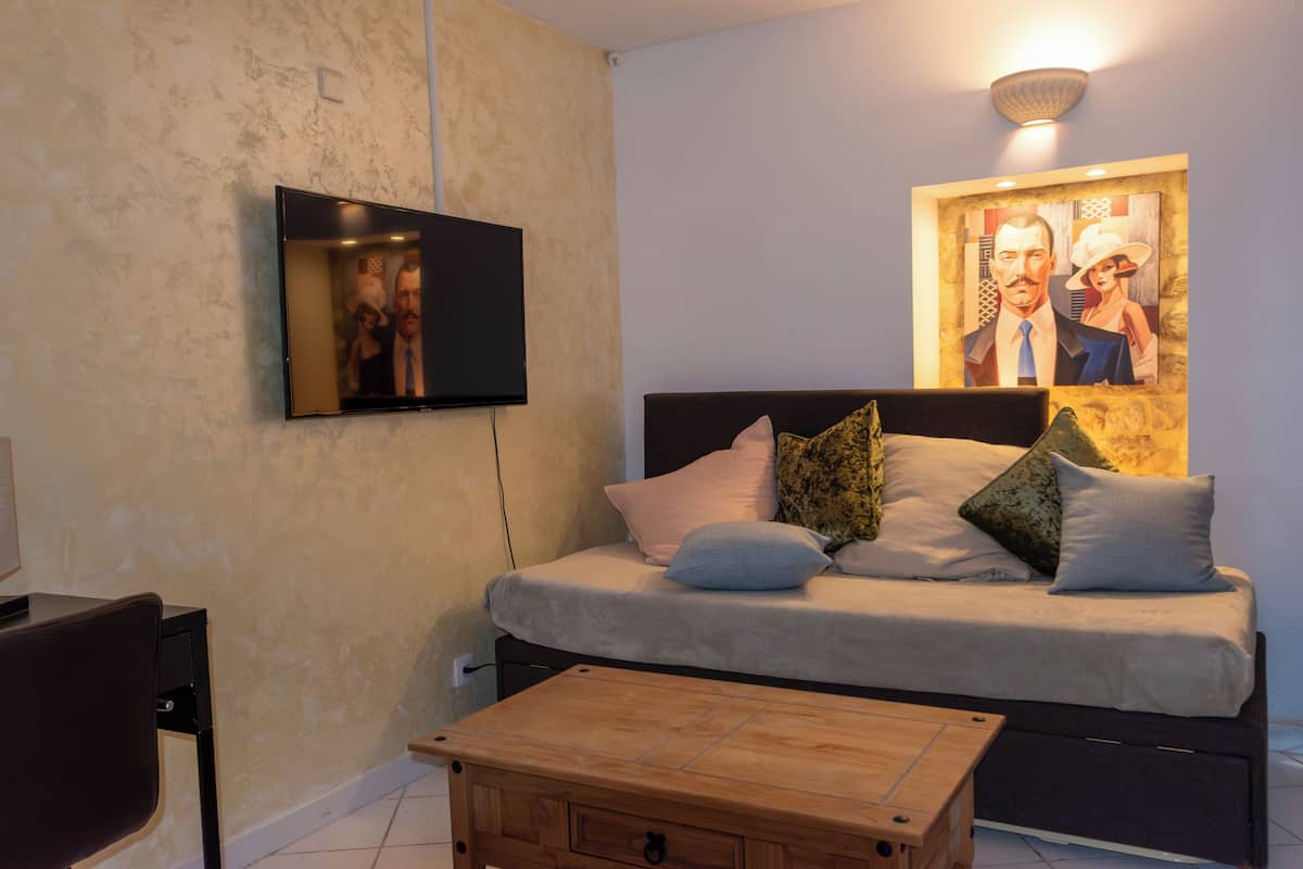 A bedroom with a bed, pillows, a TV, and a wooden coffee table.