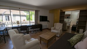 A living room with a sofa, armchairs, a coffee table, a TV, and a dining area with chairs and a table. - A L'OMBRE DU PALAIS (Avignon)
