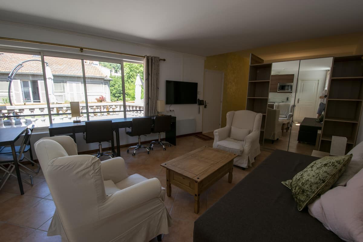 A living room with a sofa, armchairs, a coffee table, a TV, and a dining area with chairs and a table.