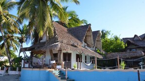 A beachfront property with thatched-roof structures, a staircase leading to the entrance, and a blue wall. - Villa Valiha Lodge (Nosy Be)