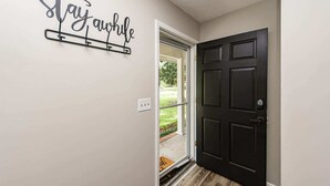 A hallway with a black door, a glass door leading outside, and a wall-mounted sign that says "Stay awhile". - Charming 3-Bedroom Retreat with Private Yard (Charleston)