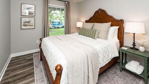 A bedroom with a wooden bed, a nightstand with a lamp, and a window with curtains. - Charming 3-Bedroom Retreat with Private Yard (Charleston)