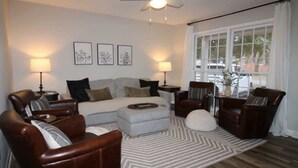 A living room with a sofa, two armchairs, a coffee table, and a rug. There is a ceiling fan, a window with curtains, and framed artwork on the wall. - Charming 3-Bedroom Retreat with Private Yard (Charleston)