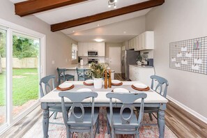 A dining area with a table set for six, surrounded by chairs, in a modern kitchen with white cabinets and a large window.