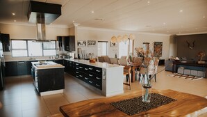 A spacious kitchen with a central island, modern appliances, and a dining area with a wooden table and chairs. - Tandweni Villa (Pongola)