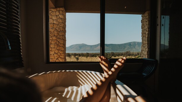 A room with a large window, stone walls, and a view of mountains. - Tandweni Villa (Pongola)