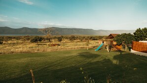 A well-maintained grassy yard with a wooden play structure and a slide, surrounded by a wooden fence and a house with a sloped roof. - Tandweni Villa (Pongola)