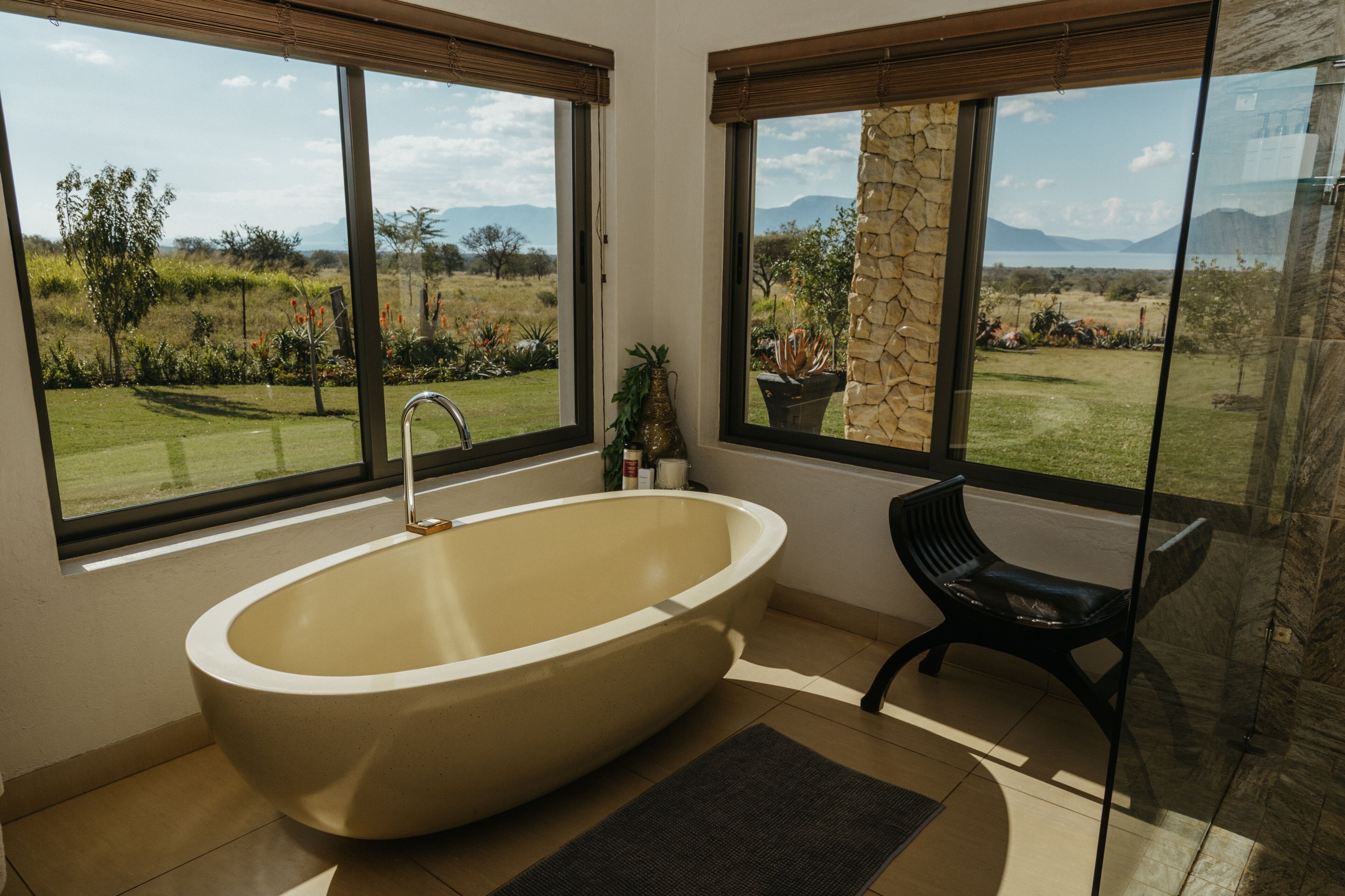 Une salle de bain moderne avec une baignoire sur pieds, de grandes fenêtres offrant une vue sur un paysage verdoyant et un pilier en pierre.
