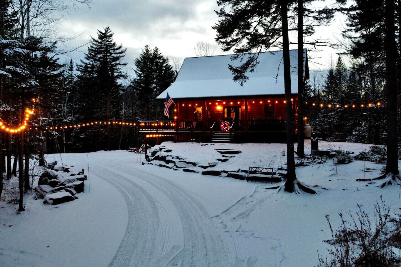 Een chalet met een oprit bedekt met sneeuw, omringd door bomen, versierd met lichtslingers.