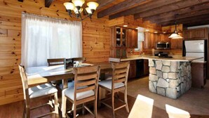 A wooden cabin interior with a dining area, kitchen, and stone island.