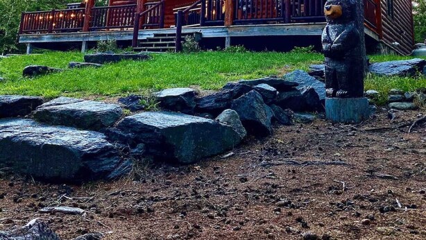 A log cabin with a porch, a bear statue, and an American flag.