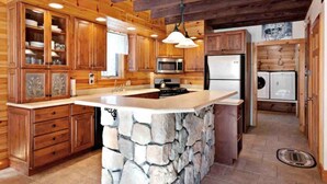 A kitchen with wooden cabinets, a stone island, a microwave, and a refrigerator.