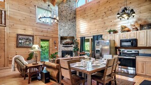 Un intérieur de chalet chaleureux avec une cheminée en pierre, un coin repas en bois et des appareils de cuisine modernes.