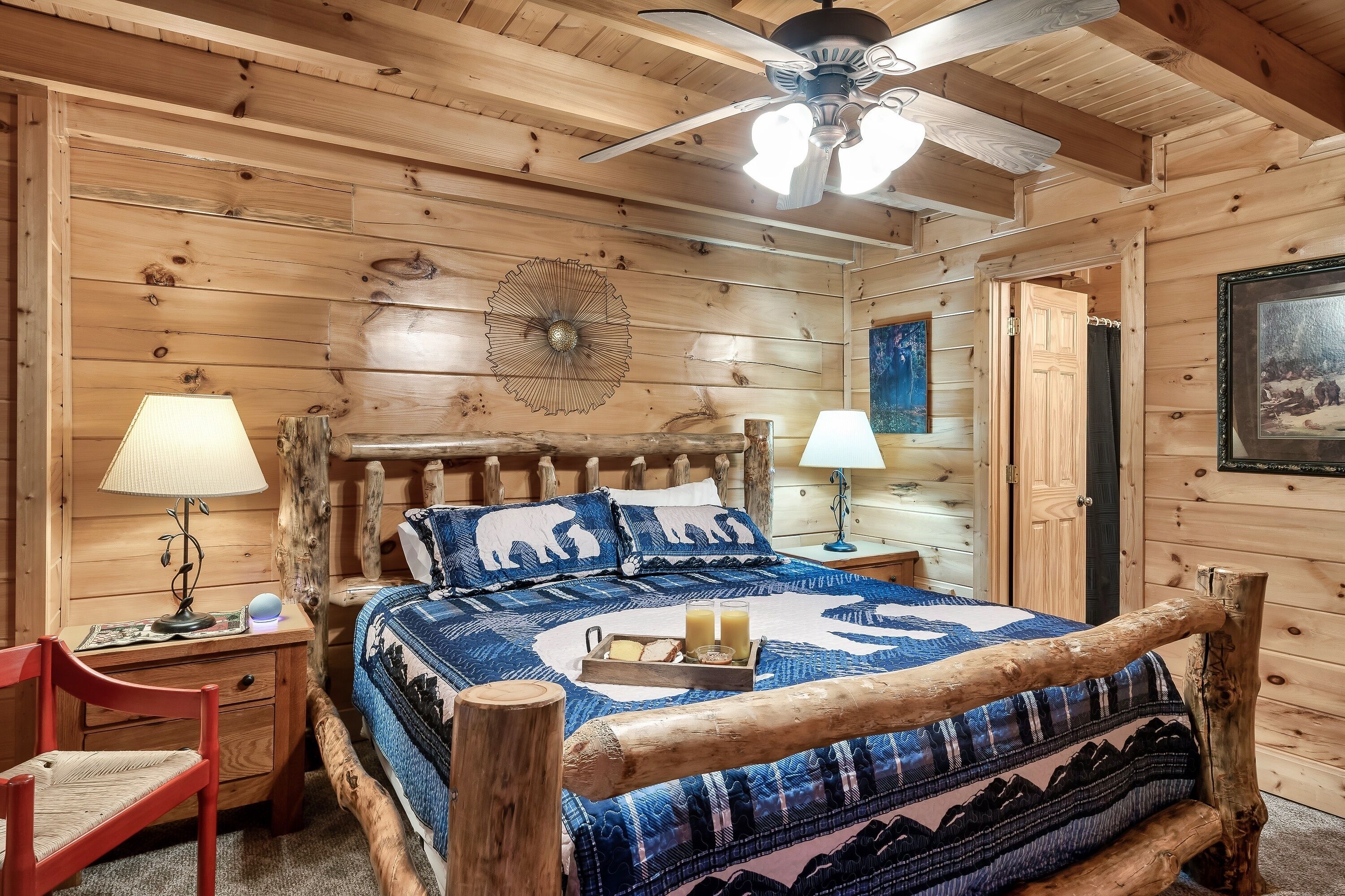Une chambre à coucher dans une cabane en bois, comprenant un lit, deux tables de chevet, une chaise, un ventilateur de plafond et un élément décoratif mural.