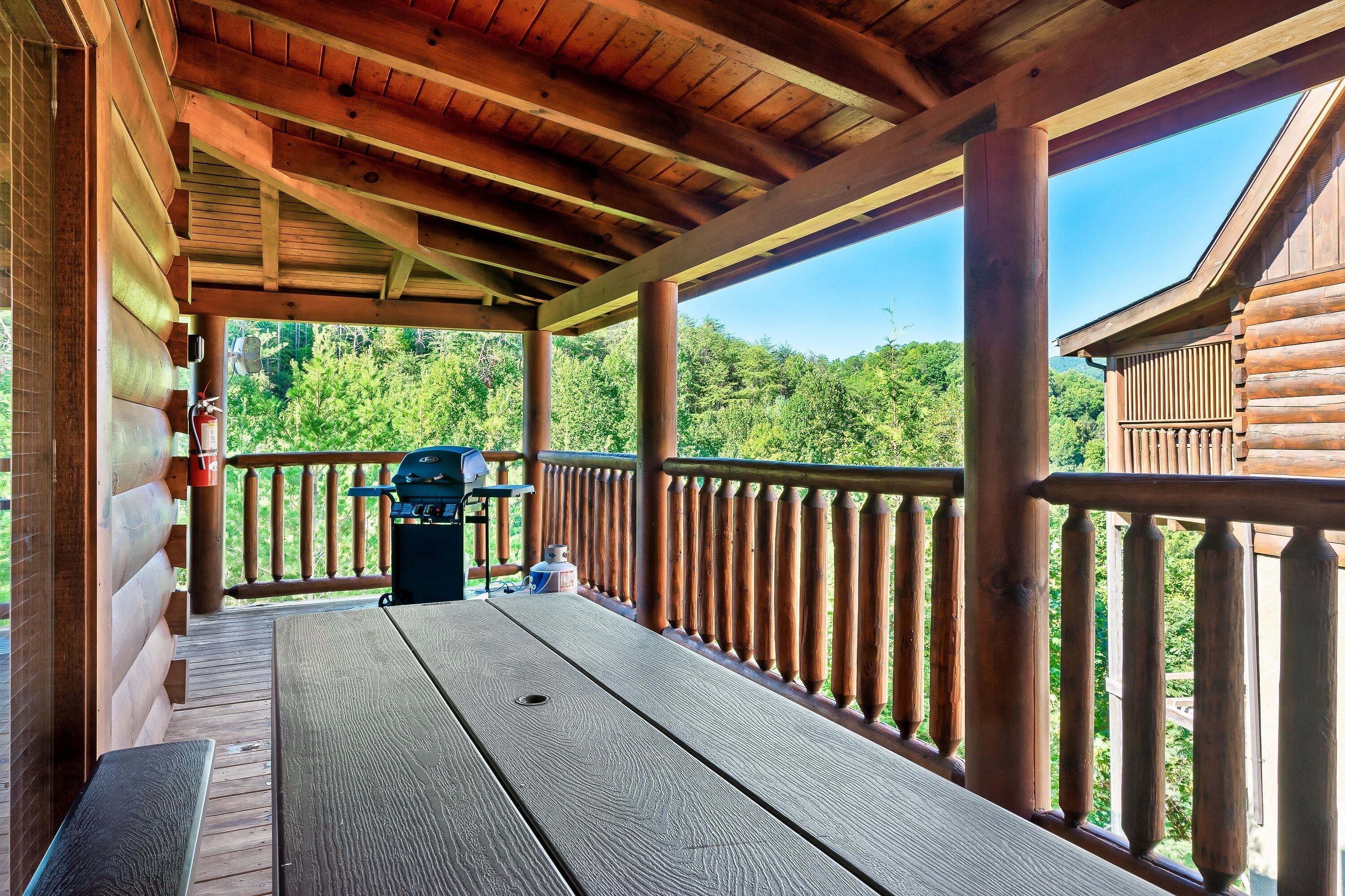 A wooden deck with a picnic table and grill, overlooking a forested area.