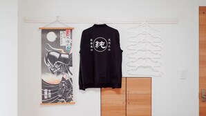 T-shirt preta com caracteres japoneses pendurada na parede, uma obra de arte emoldurada e um guarda-roupa de madeira.