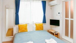 A hotel room with a bed, a television, a bedside table, and a window with curtains.