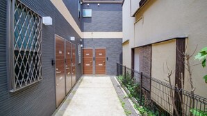 Une ruelle étroite avec un chemin en béton, des portails en métal et une clôture d’un côté.